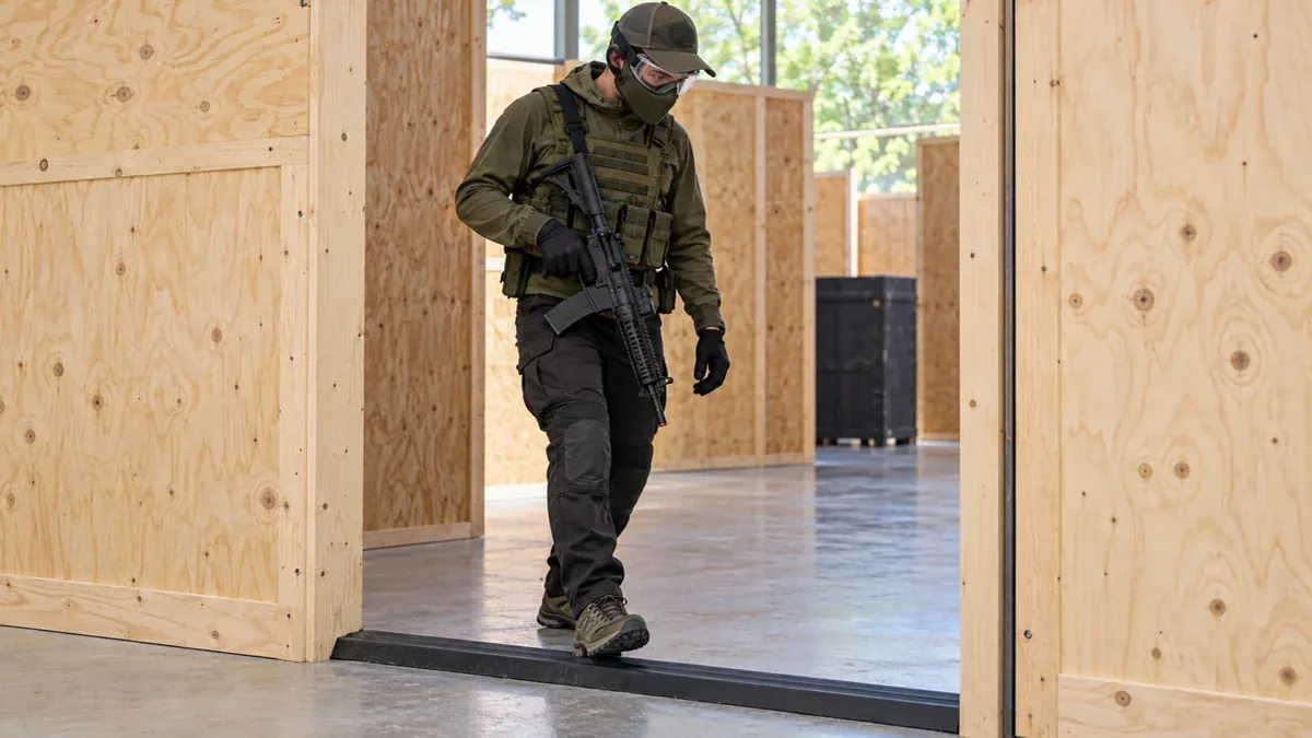 Joueur d’airsoft franchissant lentement un seuil avec des protections oculaires et faciales. Illustration générée par IA.